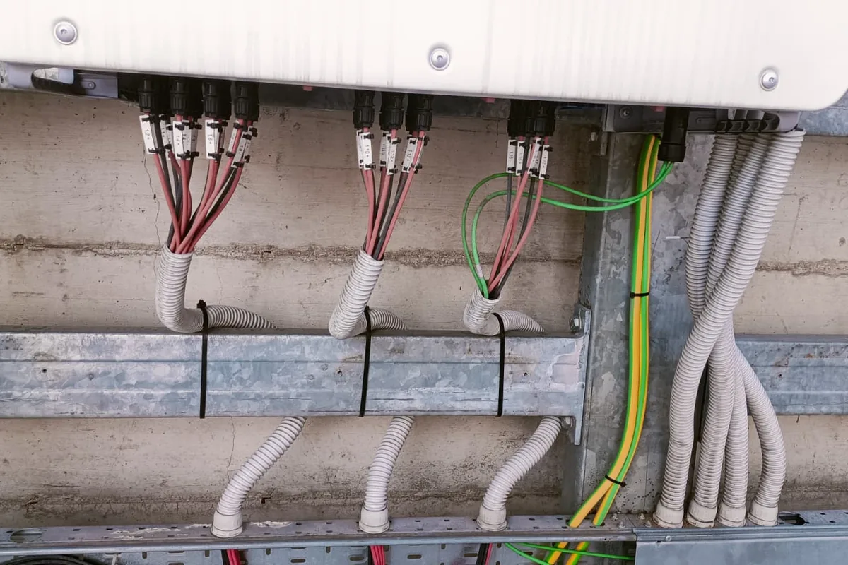 Connettori fotovoltaici attestati e siglati, con cavi ordinati in guaina corrugata, sotto un inverter di stringa