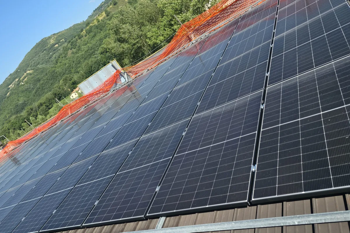 Posa di moduli fotovoltaici su copertura industriale, con rete di delimitazione del cantiere sul colmo
